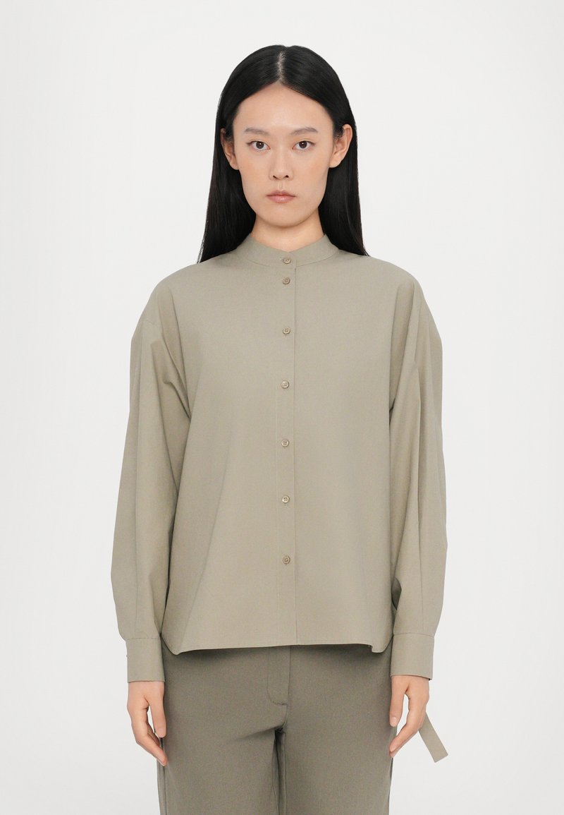 Long-sleeve, button-up shirt in light olive green. Smooth fabric, high collar, and relaxed fit with dropped shoulders and a straight hem.