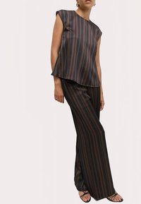 Top senza maniche a righe verticali nere e marroni con un design fluente, abbinato a pantaloni palazzo coordinati e sandali neri minimalisti.