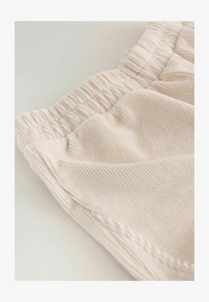 Vaalean beigekangas, jossa on uritettu pinta, joustava vyötärö ja pehmeät poimut. Yksinkertainen muotoilu, lähikuva, joka korostaa materiaalin laatua.