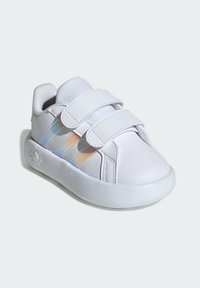 Zapatillas infantiles blancas con dos tiras de velcro, parte superior de cuero liso, tres franjas iridiscentes y una suela de goma diseñada para la comodidad.