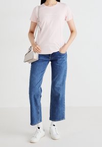 T-shirt en coton rose à manches courtes et col rond. Associé à un jean large bleu et des baskets blanches. Petit logo sur le t-shirt.