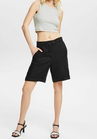 Zwarte linnen shorts met een opgerolde zoom, voorzakken en een knoopsluiting. Gepaard met een grijze crop top en zwarte hoge hakken.