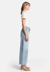 Ljust beige t-shirt med kort ärm, högmidjade ljusblå denimjeans med rak passform och gula klackskor med ormskinnsmönster.