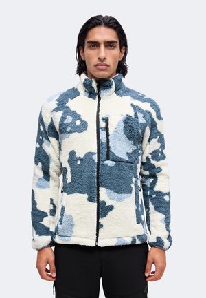 Mann trägt eine blau-weiß camouflagegemusterte Fleecejacke mit Frontreißverschluss und Reißverschlusstasche auf der Brust, steht vor einem einfarbigen Hintergrund.
