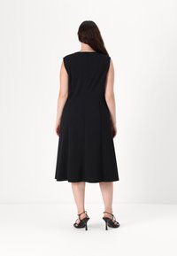 Černé šaty bez rukávů s rozšířenou sukní, hladká látka a jemné zapínání na zip na zadní straně. Spárované s černými sandály na vyšším podpatku.