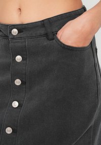 Black denim skirt featuring a fitted design, silver snap buttons down the front, and a side pocket for added functionality.
