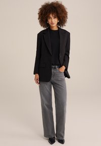 Melna žakete ar strukturētām plecu daļām, pārējo tērpu papildina teksturēts melns tops un pelēki augsti vidukļa platās bikses. Norādītās melnās kurpes ar augstiem papēžiem izceļ apģērbu.