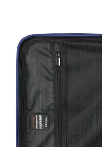 Interior de bolsa de viaje negra con un cierre azul y paneles texturizados. Presenta una pequeña etiqueta con la marca y las instrucciones de cuidado.