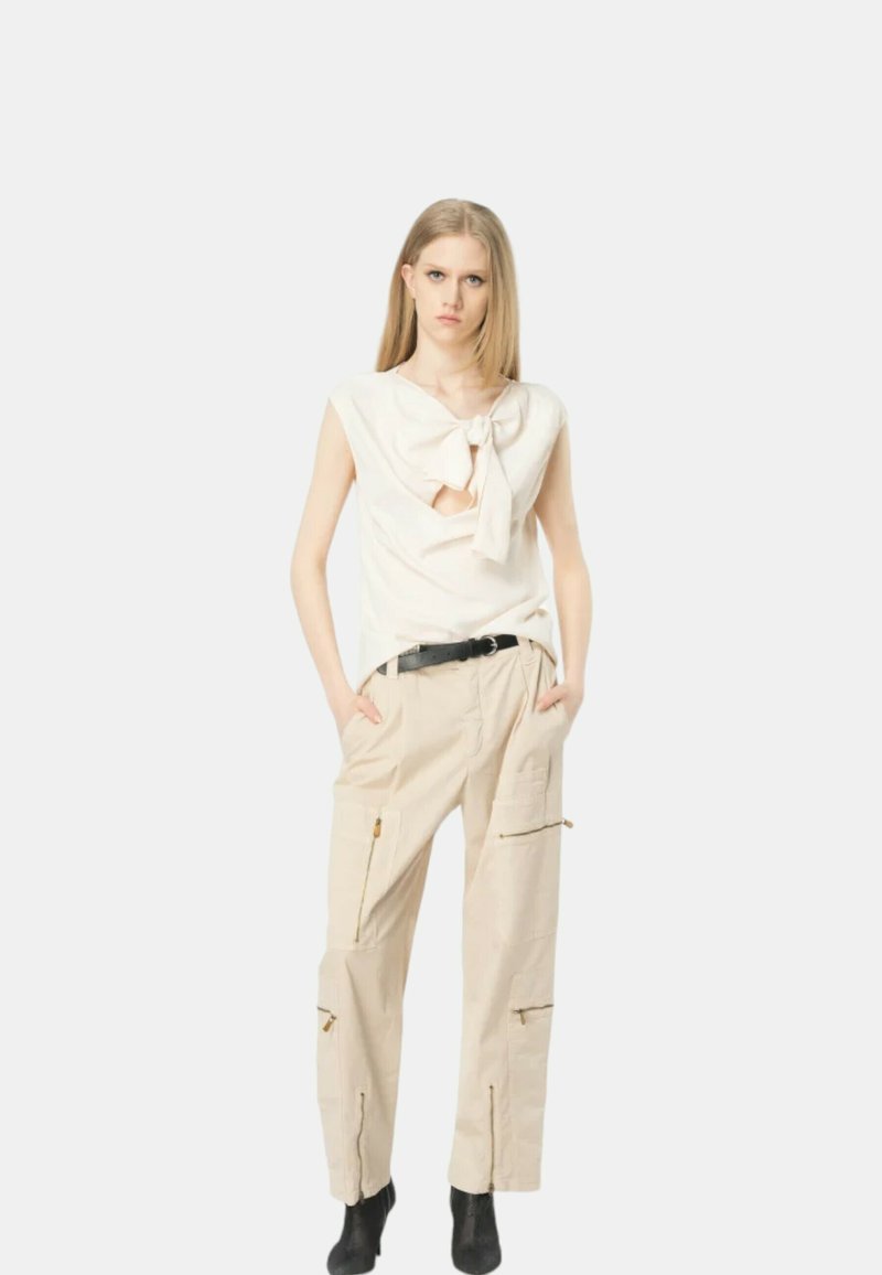 Top bianco con un dettaglio a nodo davanti, abbinato a pantaloni cargo beige con tasche con zip. Cintura nera e stivaletti alla caviglia completano il look.