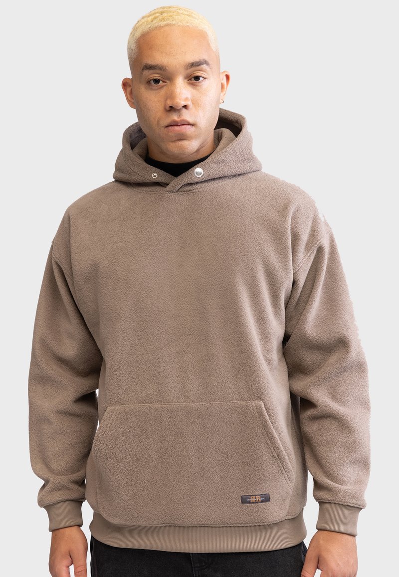 Felpa con cappuccio in beige con tasca frontale, cappuccio regolabile e polsini a coste. Presenta bottoni a pressione e un piccolo logo del marchio sull'orlo.