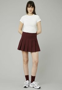 Jupe plissée bourguignonne associée à un t-shirt blanc à manches courtes, des baskets blanches et des chaussettes rouges. Design simple avec une taille ajustée.