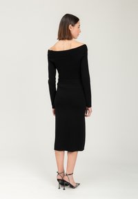 Robe en tricot noire à épaules dénudées avec des manches longues et une silhouette ajustée. Une paire de talons noirs avec une bride à la cheville et un bout pointu.