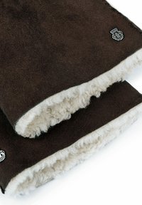 Braune Wollhandschuhe mit weißem Lammfellfutter. Sie verfügen über eine strukturierte Außenseite und ein silbernes Emblem. Die genähten Kanten fügen Detail hinzu.