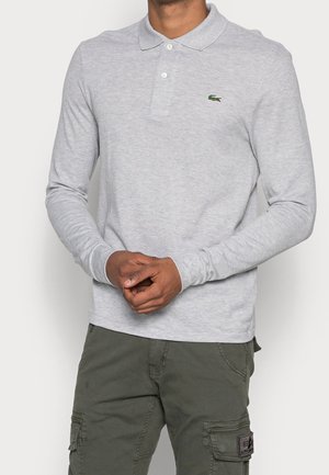 Polo à manches longues gris clair avec col et patte à trois boutons. Présente un petit logo vert sur la poitrine gauche. Texture de tissu lisse.