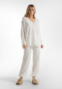 Ensemble de vêtements d'intérieur crème comprenant un haut surdimensionné avec un décolleté en V et un pantalon ample, fabriqué en tissu doux. Associé à des chaussures à enfiler beige.