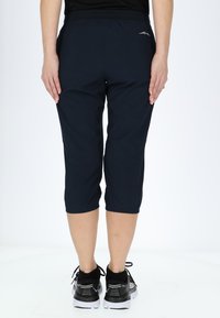 Pantaloni capri blu navy realizzati in materiale leggero, con vita elastica e polsini arricciati. Abbinati a scarpe da corsa nere.