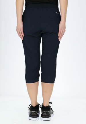 Marineblauwe capri broeken van lichtgewicht materiaal, met een elastische tailleband en gerimpelde manchetten. Gepaard met zwarte hardloopschoenen.
