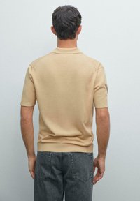 Polo shirt in maglia beige a maniche corte con colletto classico, polsini e orlo a costine, abbinato a jeans in denim grigio scuro. Tessuto strutturato.