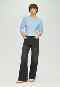 Lichtblauwe gebreide trui met lange mouwen en een brede hals, gecombineerd met zwarte wijde jeans en crèmekleurige schoenen. Eenvoudig, casual ontwerp.