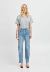 Graues Baumwoll-T-Shirt mit entspannter Passform, kombiniert mit hellblauen schmalen Jeans. Dazu flache schwarze Sandalen und minimalistische silberne Accessoires.