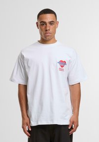 White cotton t-shirt with short sleeves, featuring a colorful graphic on the left chest area and relaxed fit design.