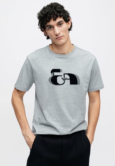 Sivé bavlnené tričko s krátkymi rukávmi, na prednej strane čierny abstraktný vzor. Okrúhly výstrih, mäkká textúra, voľný strih.