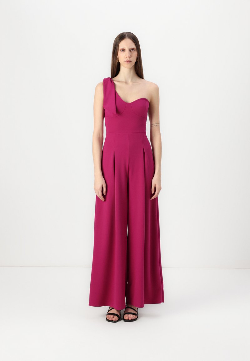 Fuchsia, en-skulder jumpsuit med plisserte vide ben og strukturert liv. Glatt materiale med matt finish, kombinert med svarte sandaler.