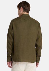 Camisa de manga larga verde oliva en una tela texturizada; cuenta con un canesú trasero, puños con botones y un dobladillo curvado.