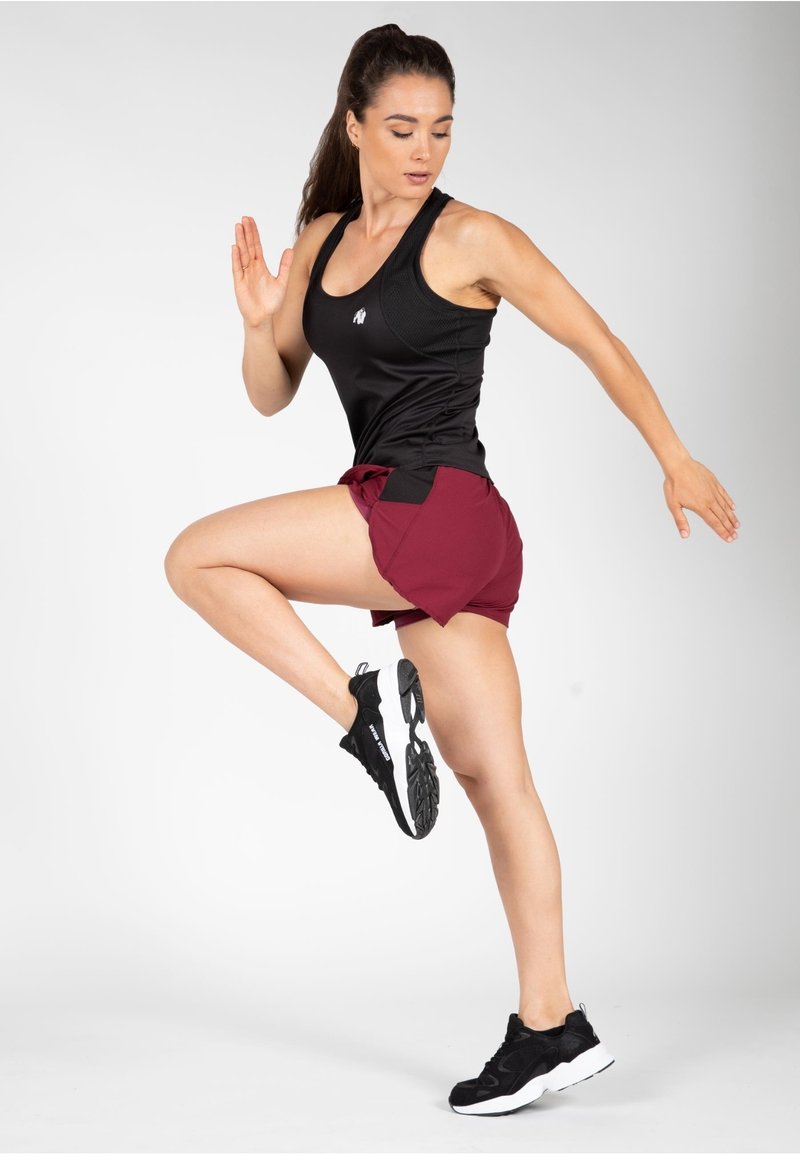 Zwarte sportieve tanktop gecombineerd met bordeauxrode shorts en zwarte sneakers. De outfit heeft contrasterende kleuren en een aangesloten ontwerp voor actieve beweging.