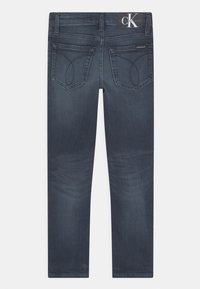 Jeans de ganga de lavagem escura com uma silhueta ajustada, dois bolsos traseiros com detalhes de costura curva e uma etiqueta Calvin Klein na cintura.