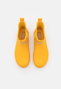 Κίτρινες αδιάβροχες μποτες μέχρι τον αστράγαλο με λεία καπίλ, ελαστικές πλευρικές πλάκες και μπροστινές θηλιές. Διαθέτουν λογότυπο "HUNTER" στη πλευρά.