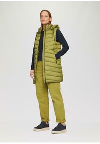 Gilet imbottito verde con cappuccio, con un design trapuntato. Abbinato a pantaloni cargo verde chiaro e sneakers nere con suola testurizzata.
