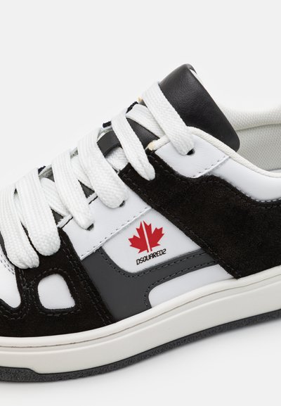 Sneaker in pelle bianca con accenti in suede neri, suola in gomma nera e lacci bianchi. Presenta un logo a foglia d'acero rossa e un design slanciato.