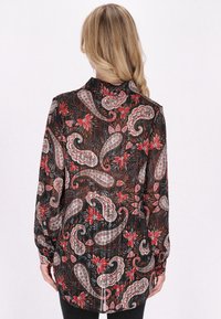 Blusa nera a maniche lunghe e trasparente con un motivo paisley in rosso, bianco e grigio. Polsini con bottoni, colletto alla mandarino e orlo curvo.