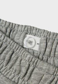 Grijze gebreide stof met een zachte textuur, met een geplooide tailleband en een doorzichtige plastic knop aan de bovenkant met een witte tab.