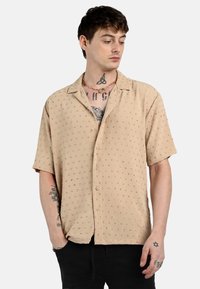 Camisa de botones de manga corta, color beige, con un patrón de puntos coloridos, fabricada en un tejido ligero, corte recto y una textura suave. Diseñada para la comodidad.