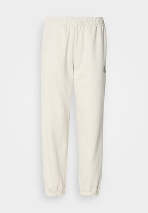 Pantalons de jogging beige clair en tissu doux, avec une taille élastique et des poignets fuselés, ornés d'un petit logo sur la jambe gauche.