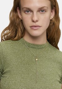 Groen geribbeld trui met een ronde hals, voorzien van een gelaagde gouden ketting met een kleine hanger, gepresenteerd op een model.