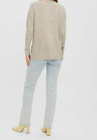 Maglione beige a maglia con orlo a coste, indossato con jeans a gamba dritta blu chiaro e scarpe con tacco a blocco gialle, visto da dietro.