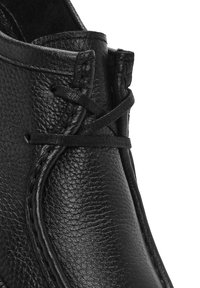 Gros plan sur la tige en cuir noir texturé d'une chaussure avec des lacets noirs noués en un nœud simple et des coutures détaillées le long des bords.