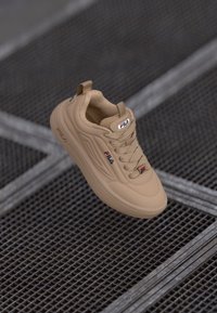 Beige FILA sneakers med en jevn, matt finish, med rund tå, teksturerte snøringer, logo detaljer og en polstret krage.