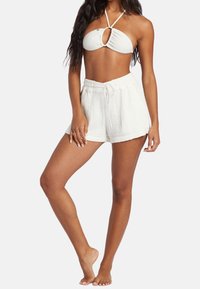 Biały bikini z fakturą i wycięciem w kształcie klucza, w połączeniu z białymi, wysokim stanem spodniami szortami z możliwością regulacji, wykonanymi z lekkiego, oddychającego materiału.