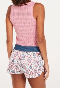 Woman wearing a pink sleeveless top and patterned shorts with a blue woven belt, shown from the back against a white background.