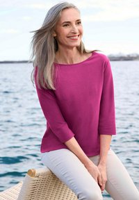 Fuchsia langemouwtop met een boot hals, zachte stof en driekwart mouwen, gecombineerd met lichtgekleurde broeken.