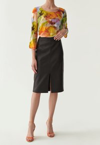 Haut en tissu transparent à motifs floraux colorés, avec des manches 3/4, associé à une jupe crayon en cuir noir avec une fente à l'avant. Sandales à talons strappy orange.