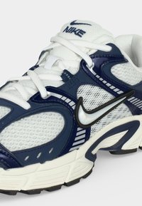 Άσπρο και ναυτικό μπλε παπούτσι τρεξίματος Nike με διχτυωτά τμήματα, χοντρή σόλα, μαύρο και άσπρο λογότυπο Nike και άσπρα κορδόνια.