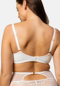 Soutien-gorge blanc avec des bretelles ajustables et un système de fermeture à crochets au dos. Il présente une texture lisse et un accent en dentelle en bas.