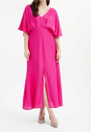 Lungo abito rosa in tessuto leggero con scollatura a V, maniche ampie e spacchi frontali, indossato con tacchi beige. Texture liscia e design fluido.