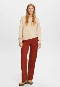 Suéter beige texturizado de manga larga, combinado con pantalones de tiro alto en color óxido. Modelo lleva unos zapatos marrones de tacón grueso.