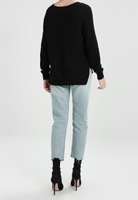 Musta neulepaita, jossa on löysä istuvuus, leveä kaula-aukko ja sivuhaarat; yhdistetty vaaleansinisiin, kuluneen näköisiin farkkuihin ja mustiin nilkkureihin, joissa on korko.